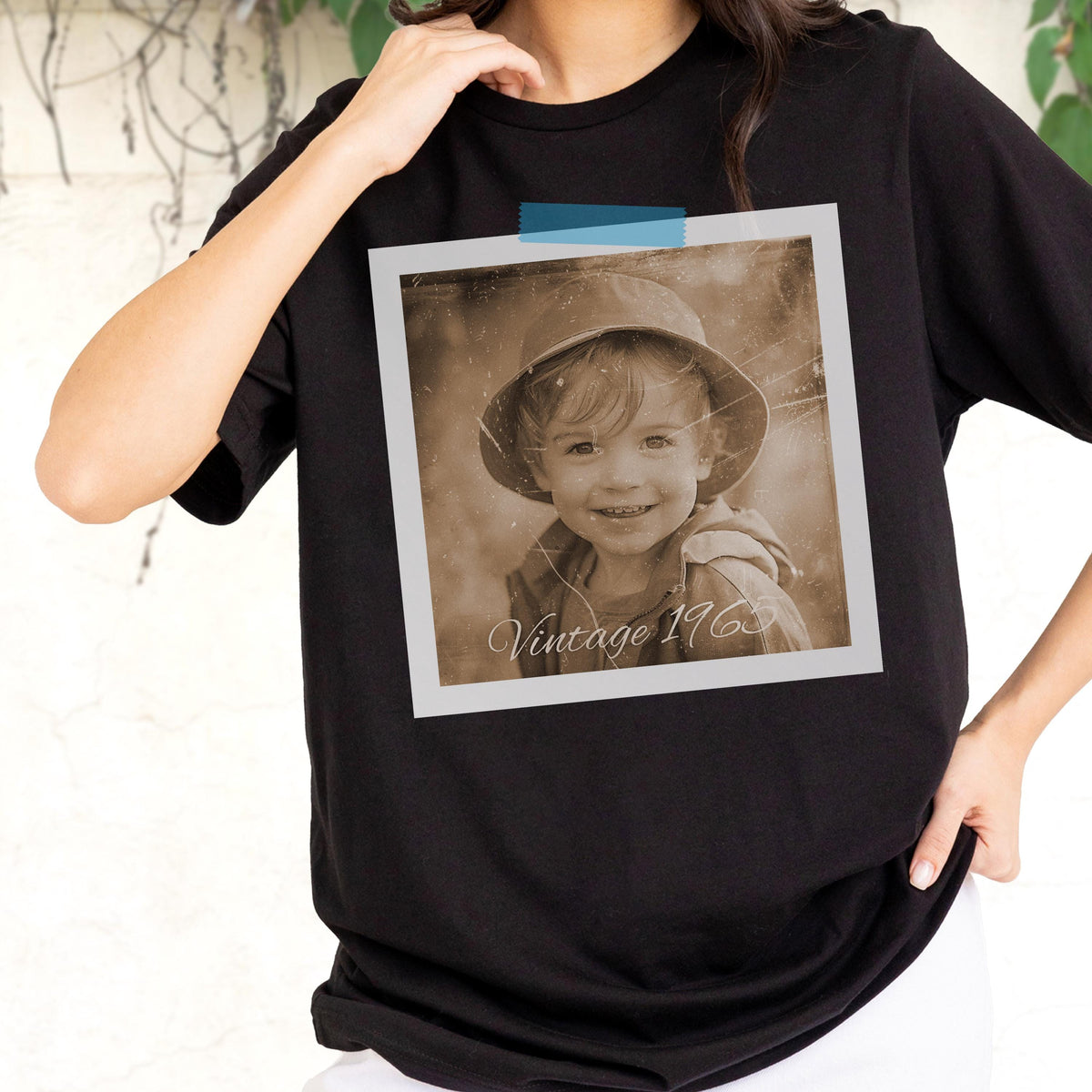 May include: Black t-shirt featuring a sepia-toned photograph of a child wearing a hat, taped to the shirt with blue tape. The photograph has the text "Vintage 1963" at the bottom. The shirt is a crew neck.