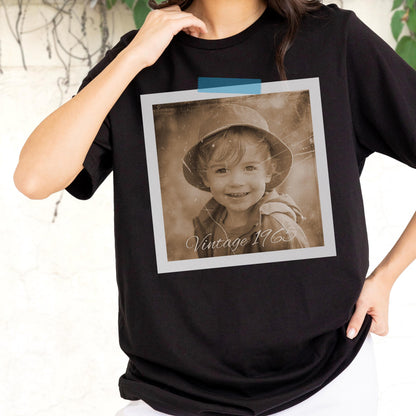 May include: Black t-shirt featuring a sepia-toned photograph of a child wearing a hat, taped to the shirt with blue tape. The photograph has the text "Vintage 1963" at the bottom. The shirt is a crew neck.