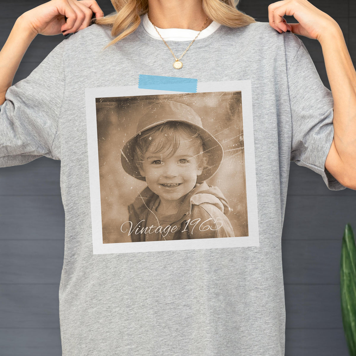 May include: A gray t-shirt featuring a sepia-toned photograph of a child wearing a hat. The photo is in a white frame and has the text "Vintage 1963" at the bottom. The shirt has a white collar.