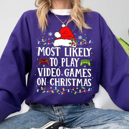 May include: A purple long-sleeve sweatshirt featuring a graphic of a Santa hat, red and green game controllers, and colorful Christmas lights. The text reads: MOST LIKELY TO PLAY VIDEO GAMES ON CHRISTMAS. The design includes small white snowflakes.