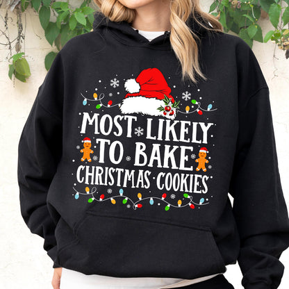 May include: A black hooded sweatshirt featuring a graphic print with a red Santa hat, two gingerbread cookies, and colorful Christmas lights. The text reads: MOST LIKELY TO BAKE CHRISTMAS COOKIES, accented with white snowflakes on the front.