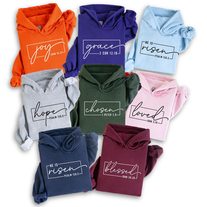 May include: A collection of hooded sweatshirts in various colors, including orange, purple, and pink. Each sweatshirt features a different inspirational word in a white rectangular frame, such as "joy," "grace," and "chosen," along with a corresponding Bible verse.