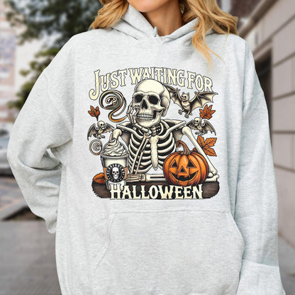 May include: A light gray hooded sweatshirt featuring a graphic print of a skeleton resting its chin on its hand next to a pumpkin and a coffee cup. The text reads "JUST WAITING FOR HALLOWEEN" with illustrations of bats and autumn leaves.