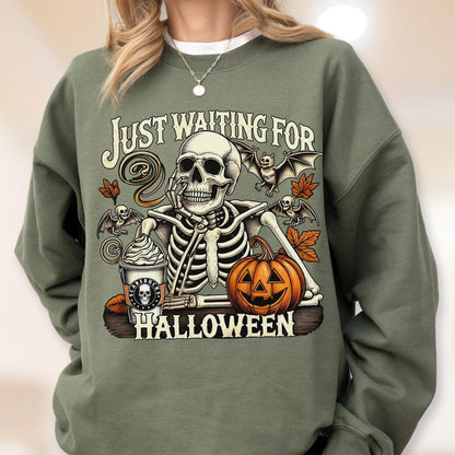 May include: An olive green crewneck sweatshirt featuring a graphic of a skeleton resting its chin on its hand. The design includes a pumpkin, bats, autumn leaves, and a coffee cup with the text "SCAREBUCKS" and "JUST WAITING FOR HALLOWEEN".