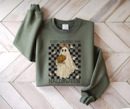 May include: Sage green sweatshirt with a Halloween-themed graphic. The graphic features a ghost holding a pumpkin, set against a checkered background with the text "JUST WAITING FOR HALLOWEEN".
