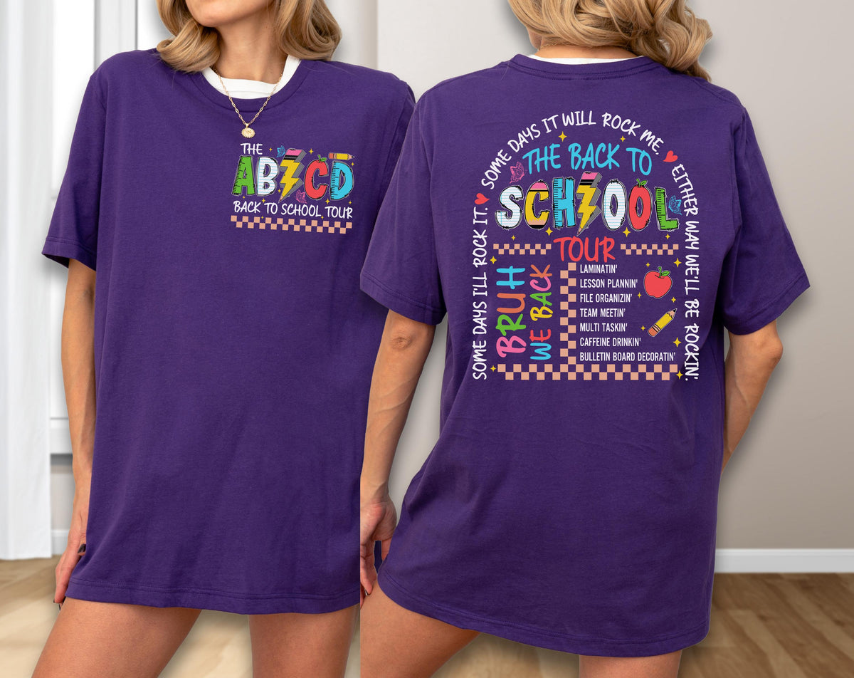 May include: A purple t-shirt with a white collar featuring the text "THE ABZCD BACK TO SCHOOL TOUR" on the front. The back of the shirt has the text "THE BACK TO SCHOOL TOUR" and other school-related phrases and graphics.