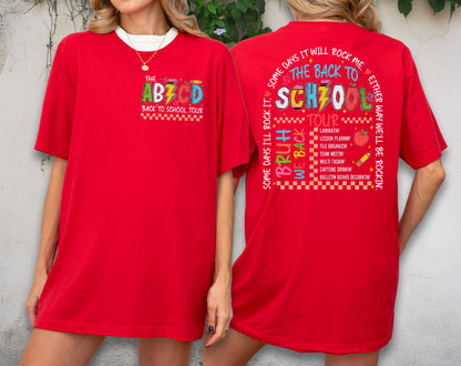 May include: A red t-shirt with the text "THE ABZCD BACK TO SCHOOL TOUR" on the front and a list of school-related activities on the back. The shirt has a white collar and a relaxed fit.