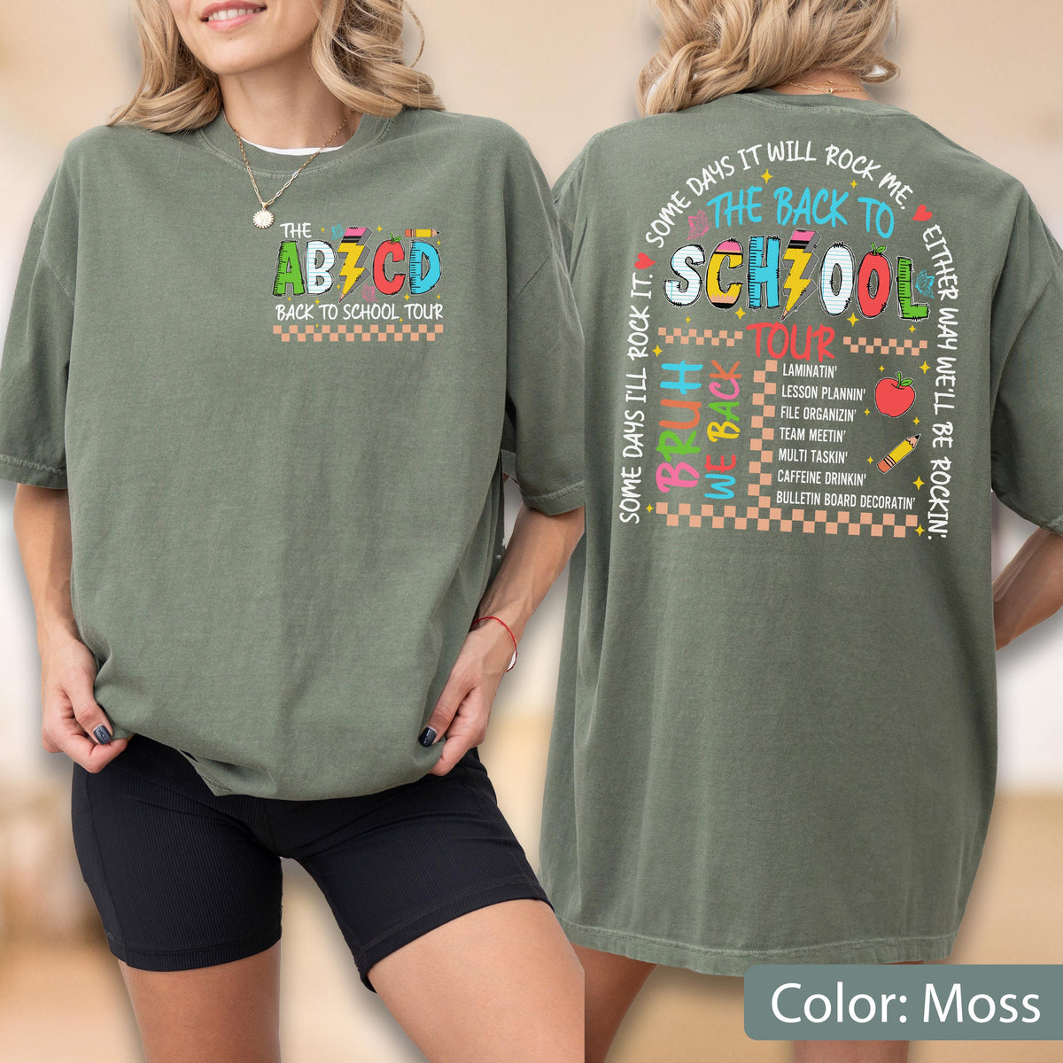 May include: Moss green t-shirt with a colorful "The ABCD Back to School Tour" graphic on the front. The back of the shirt features a school-themed design with text and icons. The shirt is made of a soft material.