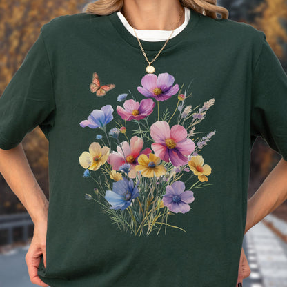 May include: A dark forest green t-shirt featuring a central graphic of a colorful wildflower bouquet in shades of pink, yellow, blue, and purple, accompanied by a single orange butterfly hovering near the top left of the floral arrangement.