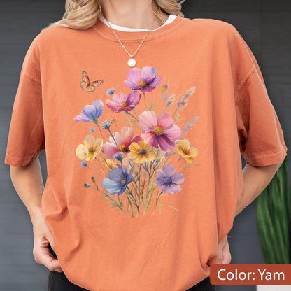 May include: A short-sleeved crew neck t-shirt in a solid burnt orange color. The front features a printed graphic of a colorful wildflower bouquet in shades of pink, purple, yellow, and blue, accompanied by a small orange butterfly.