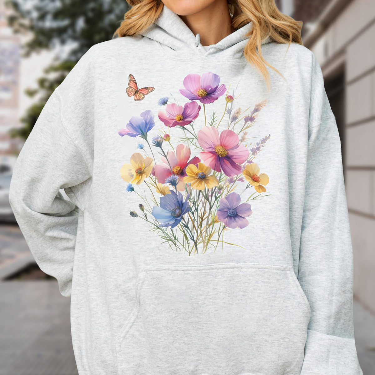 May include: A light gray hoodie featuring a watercolor floral design. The design includes a bouquet of colorful flowers in shades of pink, purple, yellow, and blue, with a small orange butterfly. The hoodie has a front pocket and a hood.