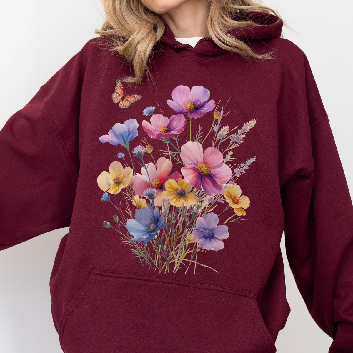 May include: Burgundy hoodie featuring a floral bouquet design with pink, yellow, and blue flowers. A small butterfly is visible near the top of the design. The hoodie has a front pocket and a hood.