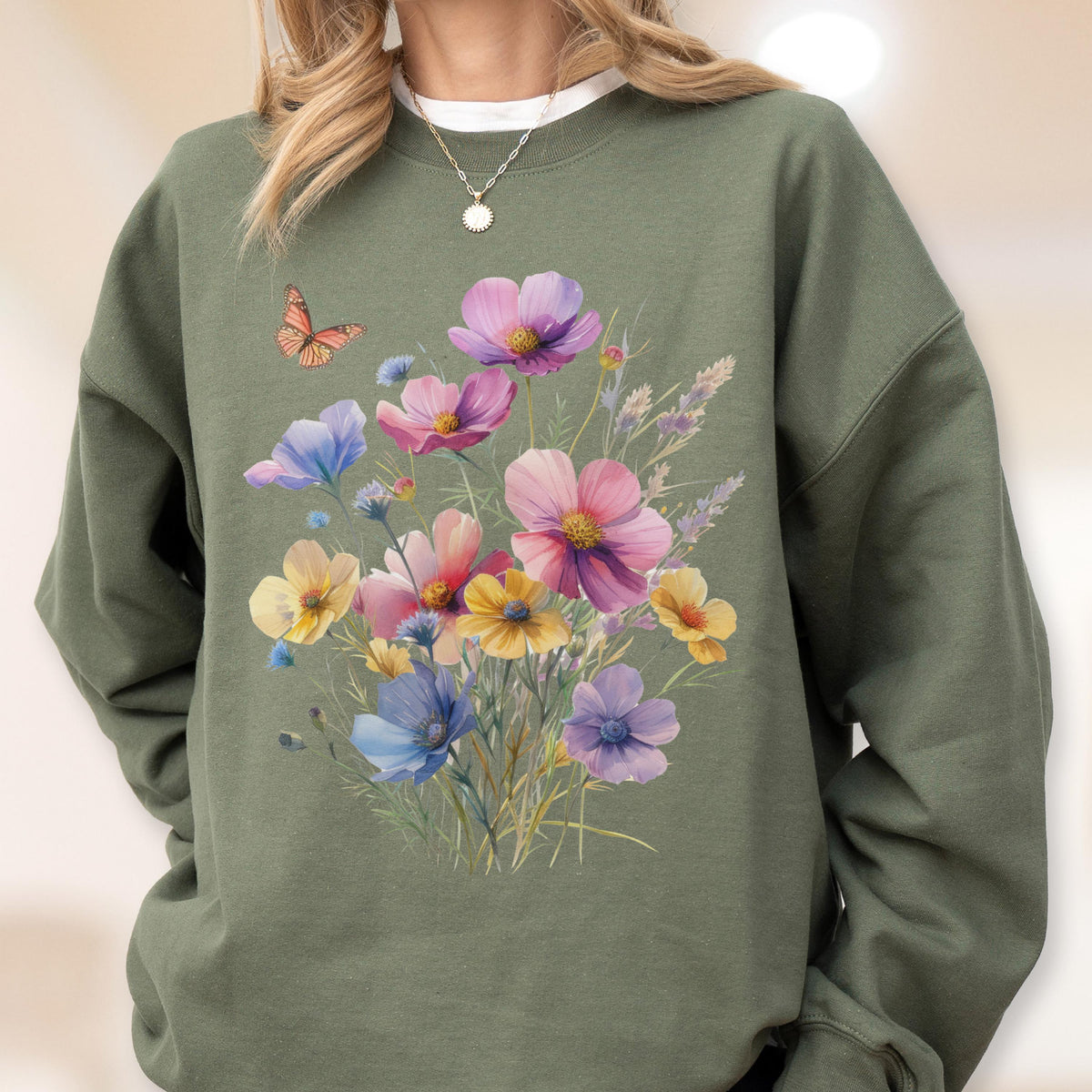 May include: Olive green sweatshirt featuring a floral design with pink, purple, yellow, and blue flowers. A small orange butterfly is on the left side of the sweatshirt. The sweatshirt has a crew neck and long sleeves.