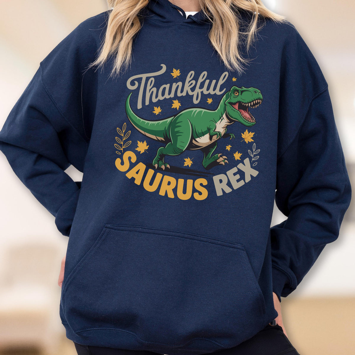 May include: Navy blue hoodie with a green dinosaur graphic and the text "Thankful Saurus Rex" in a circular design. The dinosaur is surrounded by yellow leaves and a sprig of leaves.