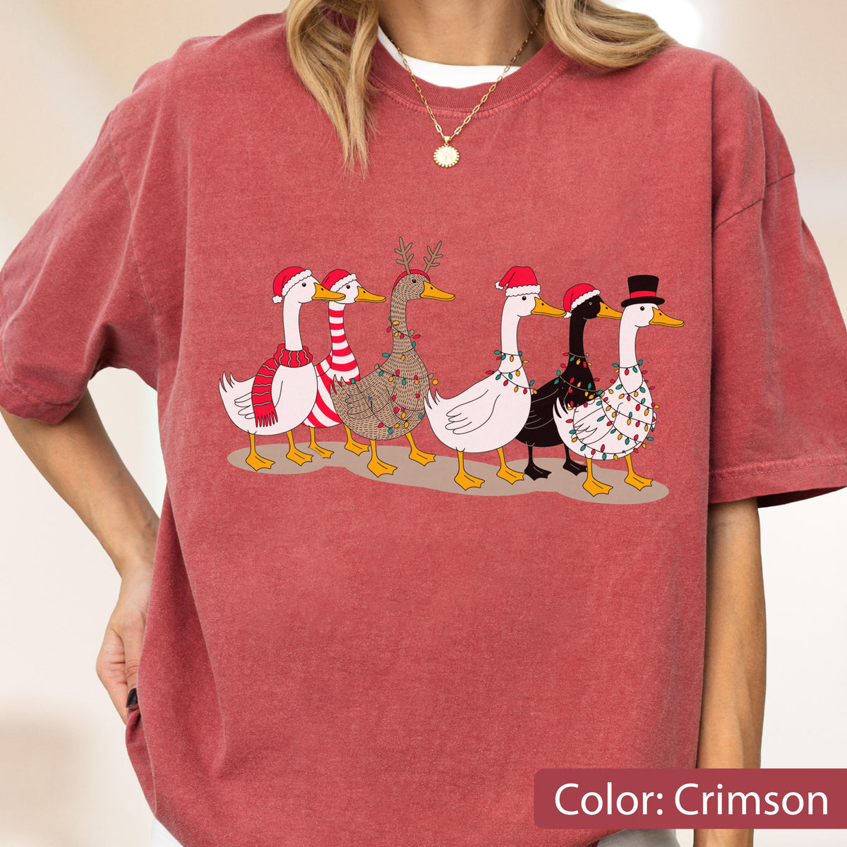 May include: A crimson short-sleeve t-shirt featuring a graphic of six geese decorated for the holidays. The geese wear various accessories including Santa hats, a red and white striped scarf, reindeer antlers, and strings of colorful Christmas lights.