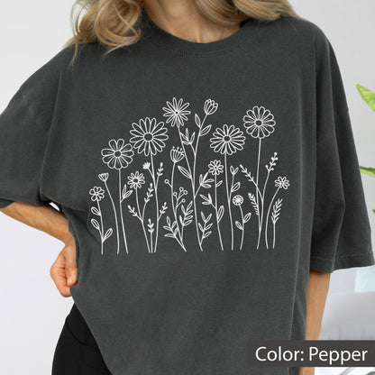 May include: A charcoal gray short-sleeved t-shirt featuring a white line art graphic of various wildflowers and stems across the center. The shirt has a crew neckline and a relaxed fit, with the color labeled as pepper in the bottom corner.