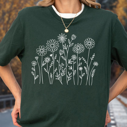 May include: A dark forest green short-sleeved t-shirt featuring a white line art graphic of a variety of wildflowers and stems across the front. The shirt has a crew neckline and is worn with a simple gold-toned chain necklace.