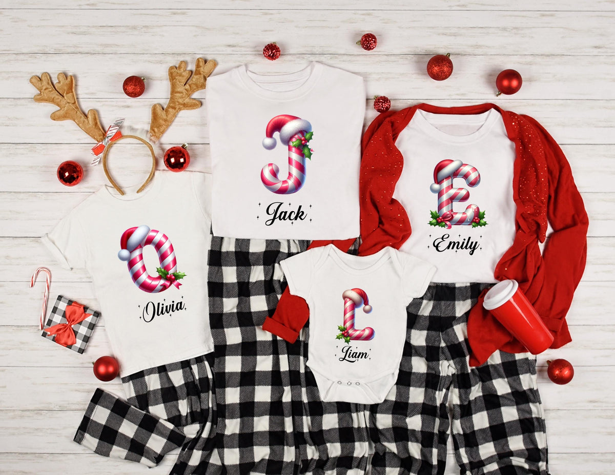May include: White Christmas-themed shirts and pajamas with candy cane letter designs. The shirts feature the names "Jack", "Olivia", "Emily", and "Liam". The pajamas are black and white checkered.