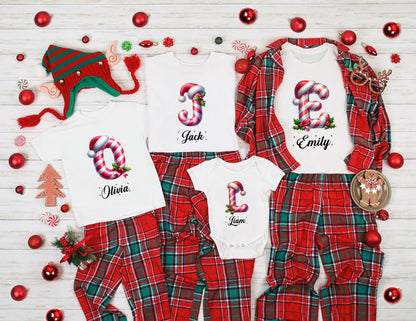 May include: A family Christmas pajama set featuring white tops with candy cane letter designs and names, paired with red and green plaid pants. Includes a matching elf hat and festive decorations.