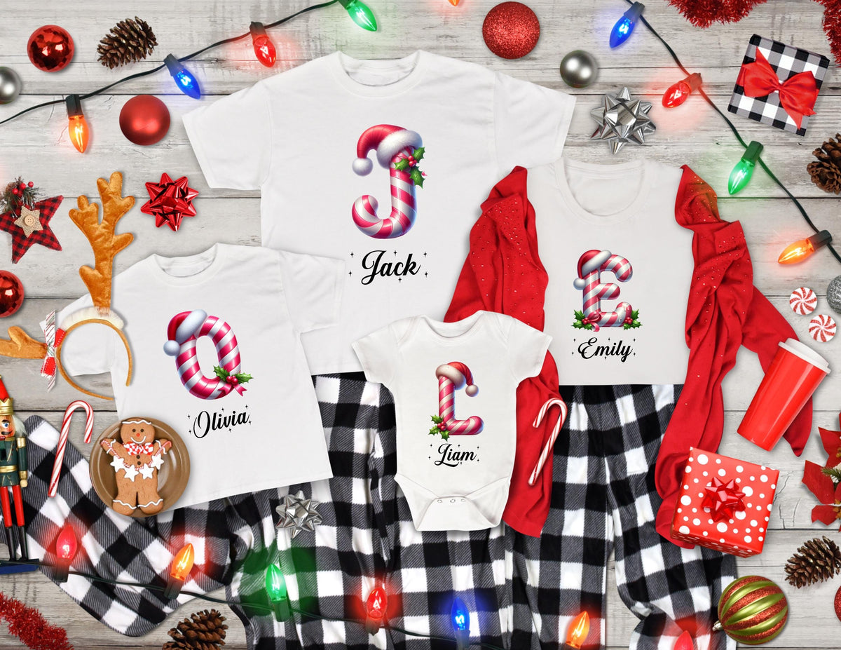 May include: White Christmas-themed family pajamas. The shirts feature candy cane letters with names: Jack, Olivia, Emily, and Liam. The pajamas include a onesie, a long-sleeve shirt, and two short-sleeve shirts. The bottoms are black and white plaid.