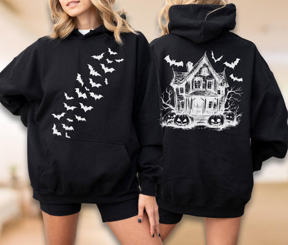 May include: A black hooded sweatshirt featuring a white graphic of a swarm of bats on the front chest. The back of the sweatshirt displays a detailed white illustration of a haunted house surrounded by bare trees and several carved jack-o'-lanterns.