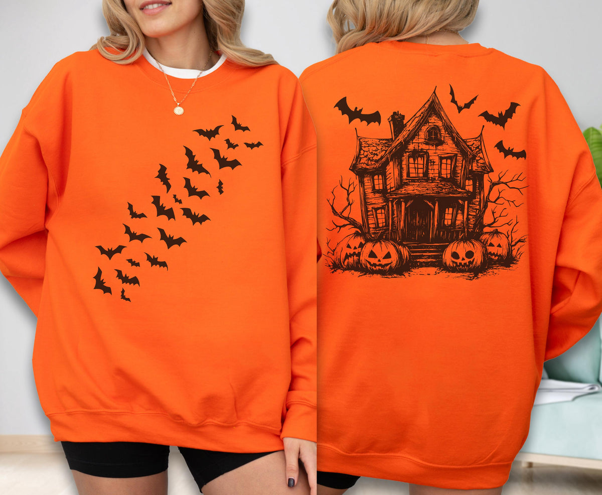 May include: An orange long-sleeve sweatshirt featuring a black graphic of a swarm of bats on the front. The back displays a detailed black illustration of a haunted house surrounded by bare trees, pumpkins, and flying bats against the orange fabric.