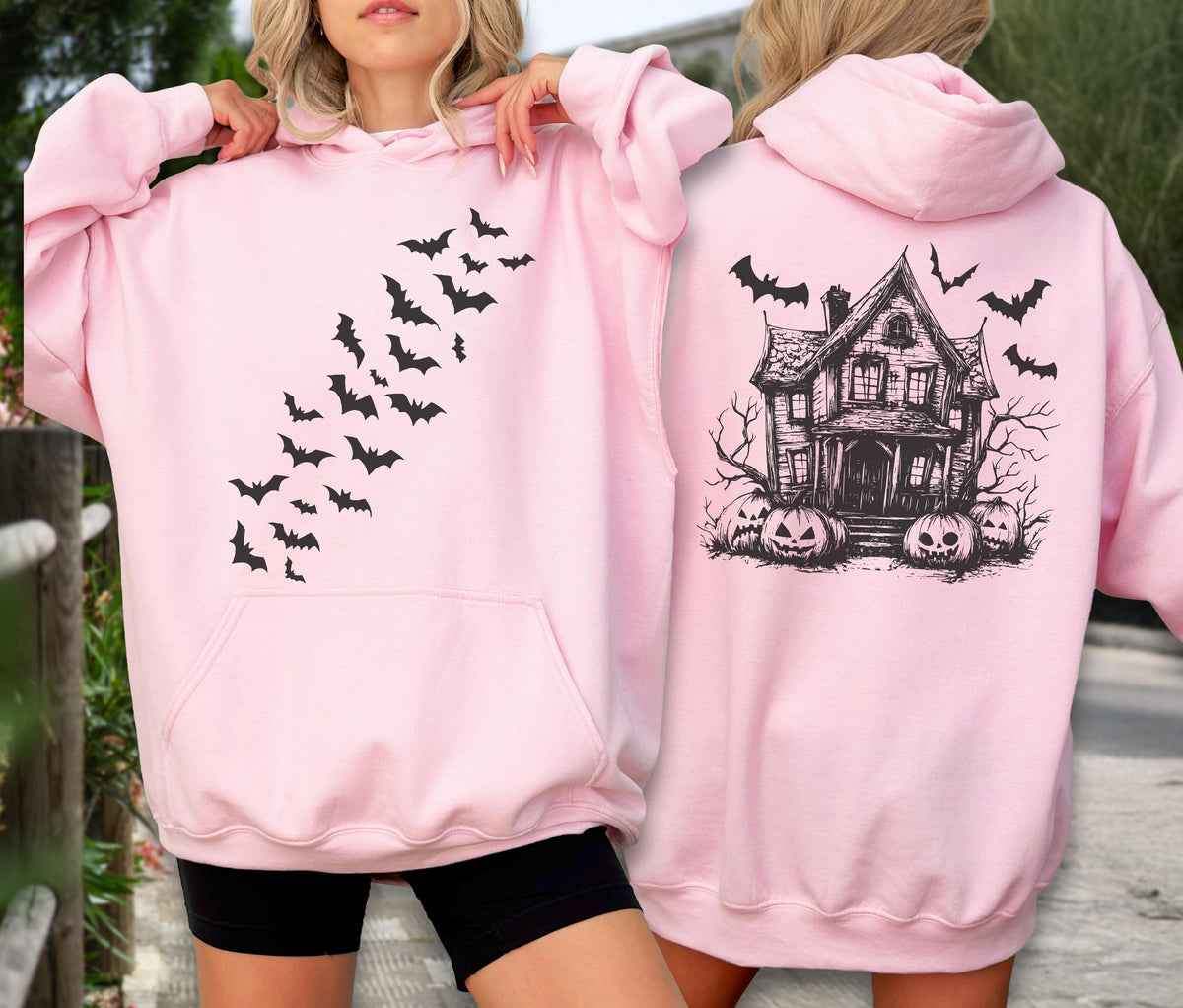 May include: A light pink hooded sweatshirt featuring a black graphic of a swarm of bats on the front. The back of the sweatshirt displays a black graphic of a haunted house surrounded by jack-o'-lanterns and additional flying bats.