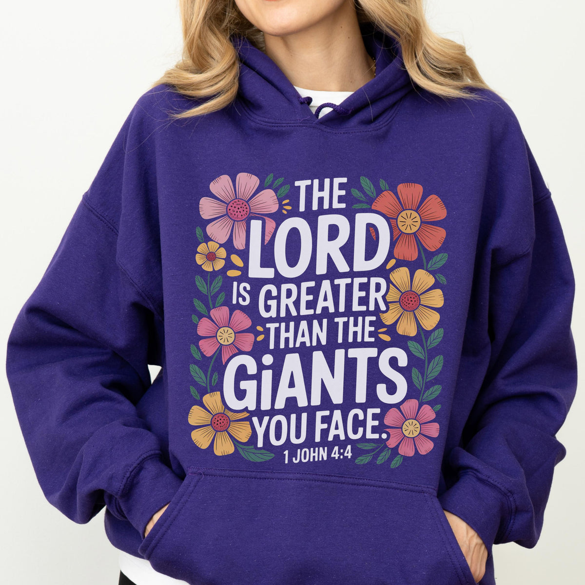 May include: A purple hoodie with a floral design and the text "THE LORD IS GREATER THAN THE GIANTS YOU FACE. 1 JOHN 4:4". The design features colorful flowers in pink, orange, and yellow.