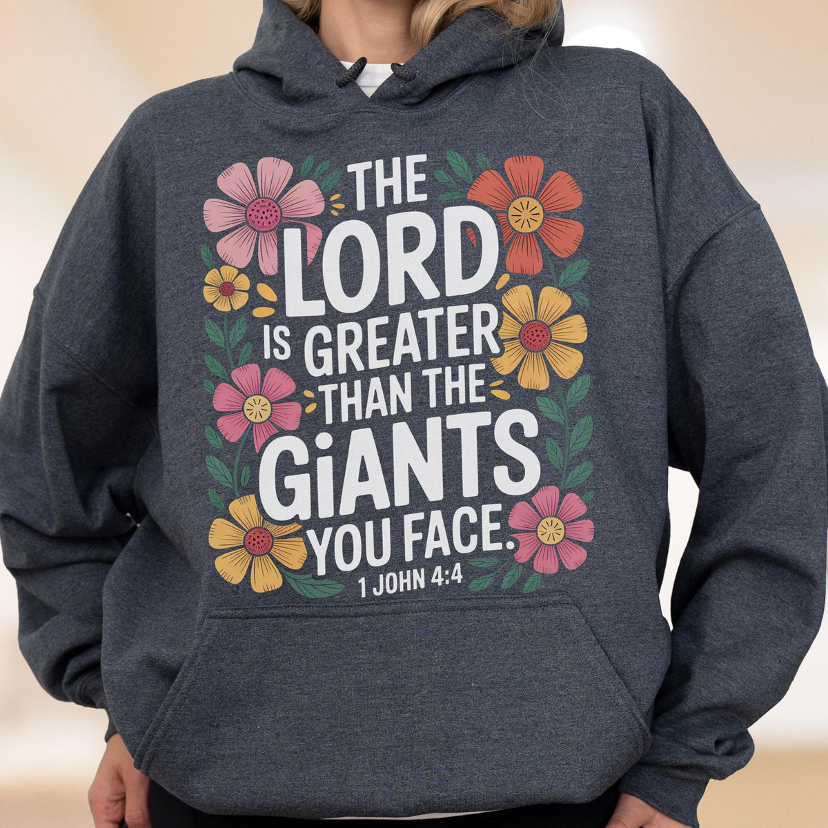 May include: A dark gray hoodie with a floral design and the text "THE LORD IS GREATER THAN THE GIANTS YOU FACE. 1 JOHN 4:4". The design features pink, yellow, and orange flowers.