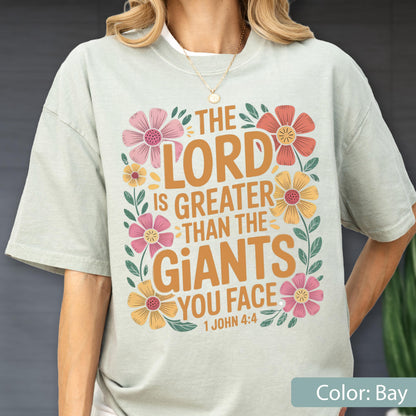 May include: A light green t-shirt with the text "THE LORD IS GREATER THAN THE GIANTS YOU FACE 1 JOHN 4:4" in orange. The text is surrounded by colorful floral illustrations in pink, yellow, and orange.