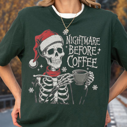 May include: Dark green t-shirt featuring a skeleton wearing a Santa hat and red scarf, holding a coffee cup. The text "NIGHTMARE BEFORE COFFEE" is printed above the skeleton. Snowflakes are also printed on the shirt.