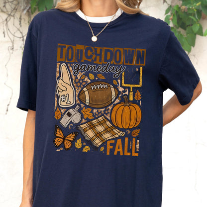 May include: Navy blue t-shirt with a football-themed graphic. The design includes a football, pumpkin, leaves, and the words "Touchdown Gameday Fall". A foam finger, whistle, and butterfly are also featured.