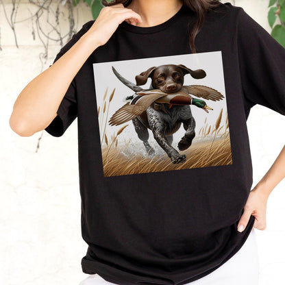 May include: Black t-shirt featuring a square graphic of a hunting dog with a duck in its mouth, running through tall grass. The dog is brown and white with floppy ears. The duck has brown and green feathers. The background is a light gray.
