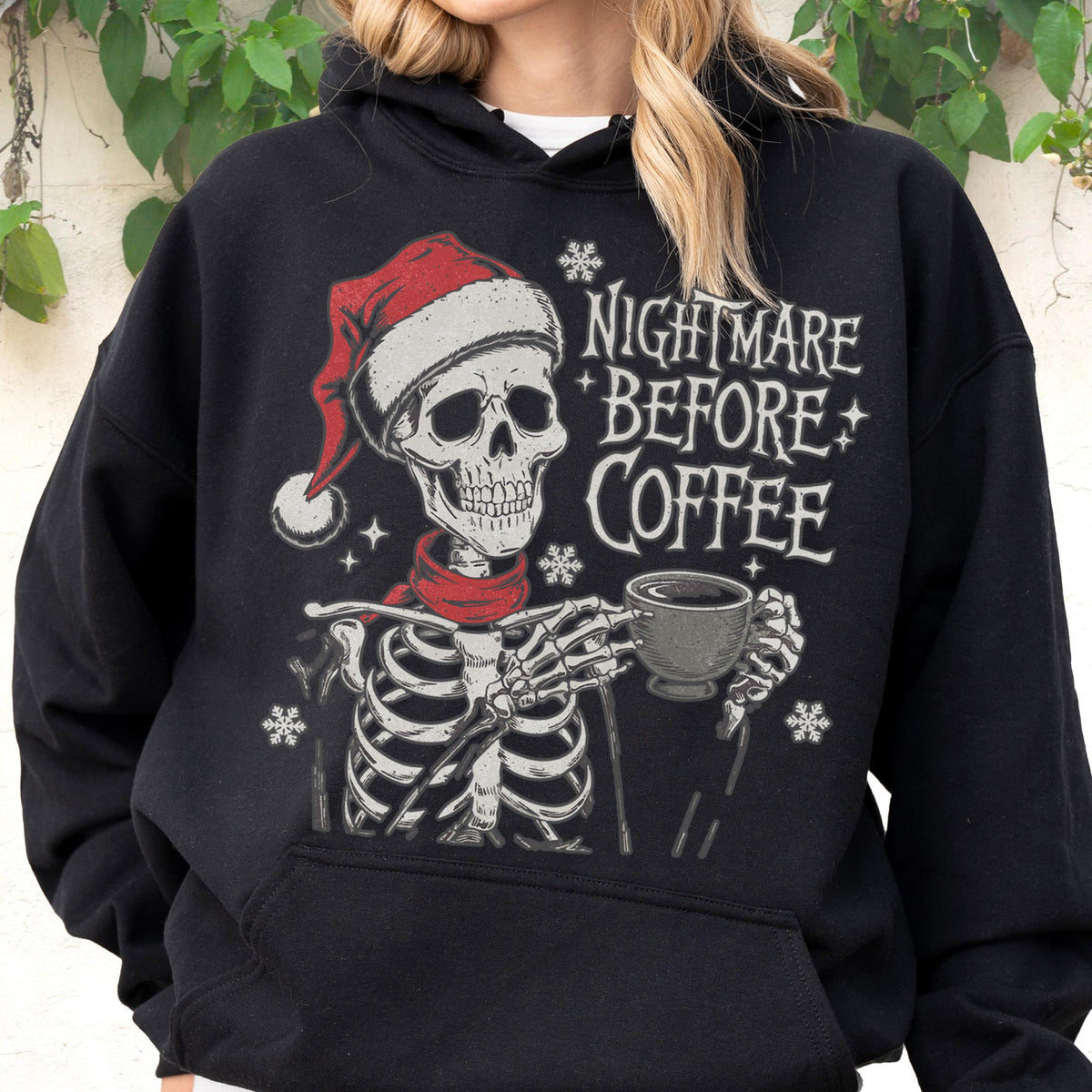 May include: Black hoodie featuring a skeleton wearing a Santa hat and red scarf, holding a coffee cup. The text "NIGHTMARE BEFORE COFFEE" is printed on the front, along with snowflake and star graphics. A festive and spooky design.