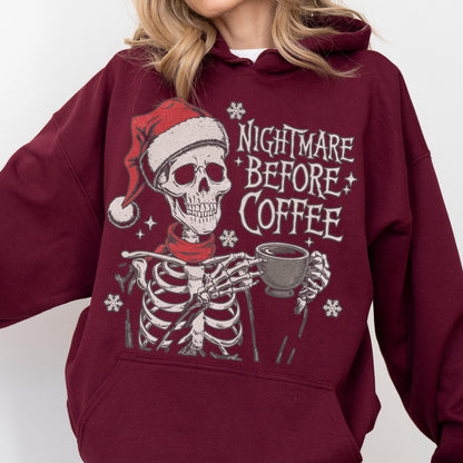 May include: Burgundy hoodie featuring a skeleton wearing a Santa hat and red scarf, holding a coffee cup. The text "NIGHTMARE BEFORE COFFEE" is printed in white. Snowflake and star graphics complete the design.