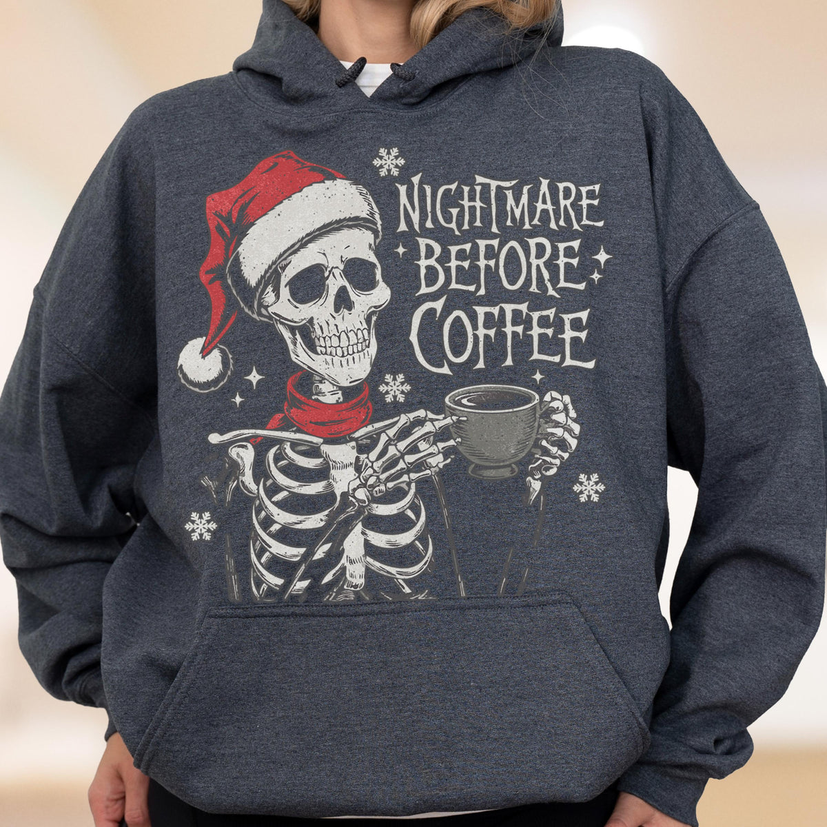 May include: Dark gray hoodie featuring a skeleton wearing a Santa hat and red scarf, holding a coffee cup. The text "Nightmare Before Coffee" is printed on the front, along with snowflake graphics. A festive and spooky design.