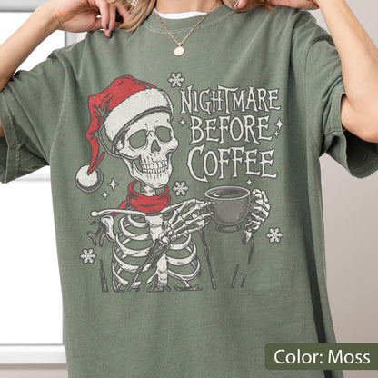 May include: Moss green t-shirt featuring a skeleton wearing a Santa hat and red scarf, holding a coffee cup. The text "NIGHTMARE BEFORE COFFEE" is printed above the skeleton. Snowflake graphics are scattered around the design.