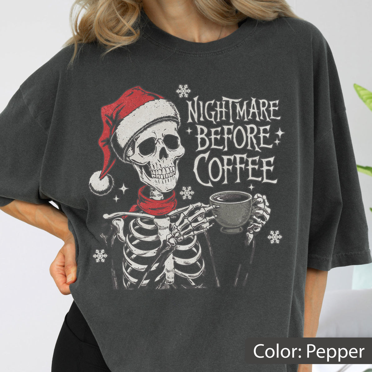 May include: Pepper-colored t-shirt featuring a skeleton wearing a Santa hat and scarf, holding a coffee cup. The text "NIGHTMARE BEFORE COFFEE" is printed above the skeleton. Snowflakes are scattered around the design.