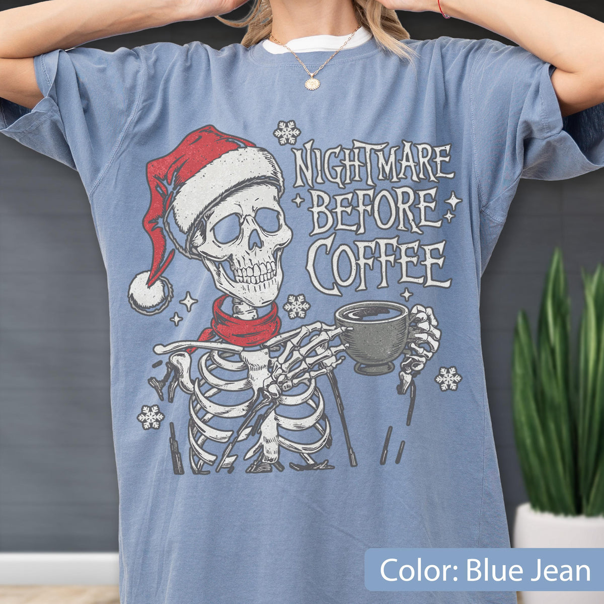 May include: Blue jean-colored t-shirt featuring a skeleton wearing a Santa hat and red scarf, holding a coffee cup. The shirt has the text "Nightmare Before Coffee" in white. The shirt is a relaxed fit.