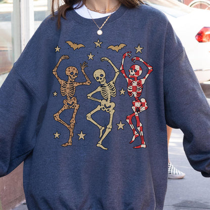 May include: A dark blue sweatshirt featuring a Halloween design. The graphic includes three dancing skeletons in various colors, bats, and stars. The skeletons are in shades of brown, beige, and red.