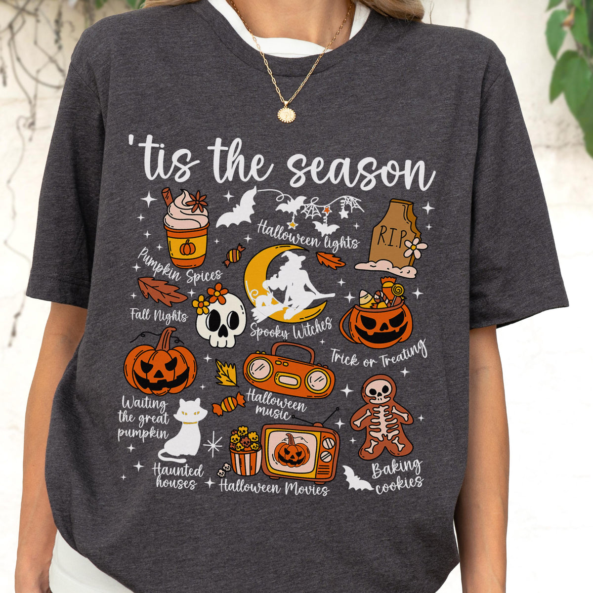 May include: Dark gray t-shirt with the phrase "'tis the season" and Halloween-themed illustrations. The design includes pumpkins, bats, a skull, and the words "Pumpkin Spices", "Spooky Witches", and "Trick or Treating".