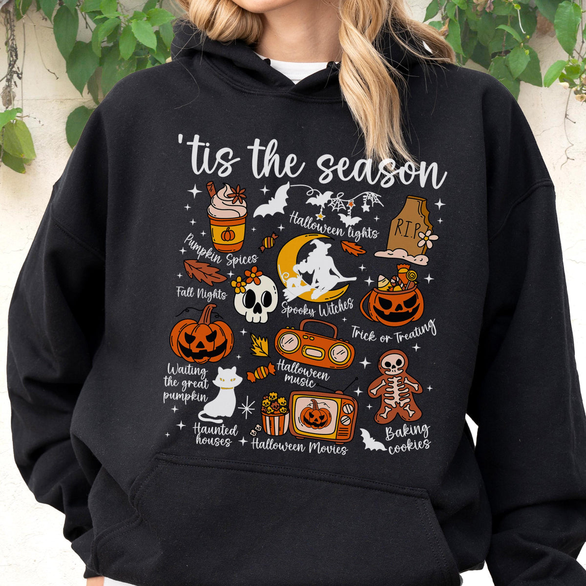 May include: Black hooded sweatshirt with a Halloween-themed graphic. The design includes pumpkins, bats, a witch, and the phrase "'tis the season." Additional text includes "Pumpkin Spices," "Halloween lights," and "Trick or Treating."