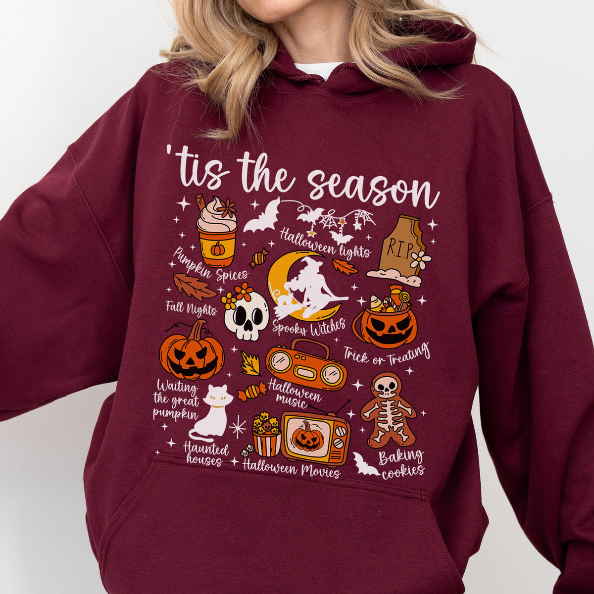 May include: Burgundy hoodie with a Halloween-themed graphic. The design includes various illustrations such as pumpkins, bats, a skull, and the phrase "'tis the season." Other text includes "Pumpkin Spices," "Halloween Lights," and "Trick or Treating."