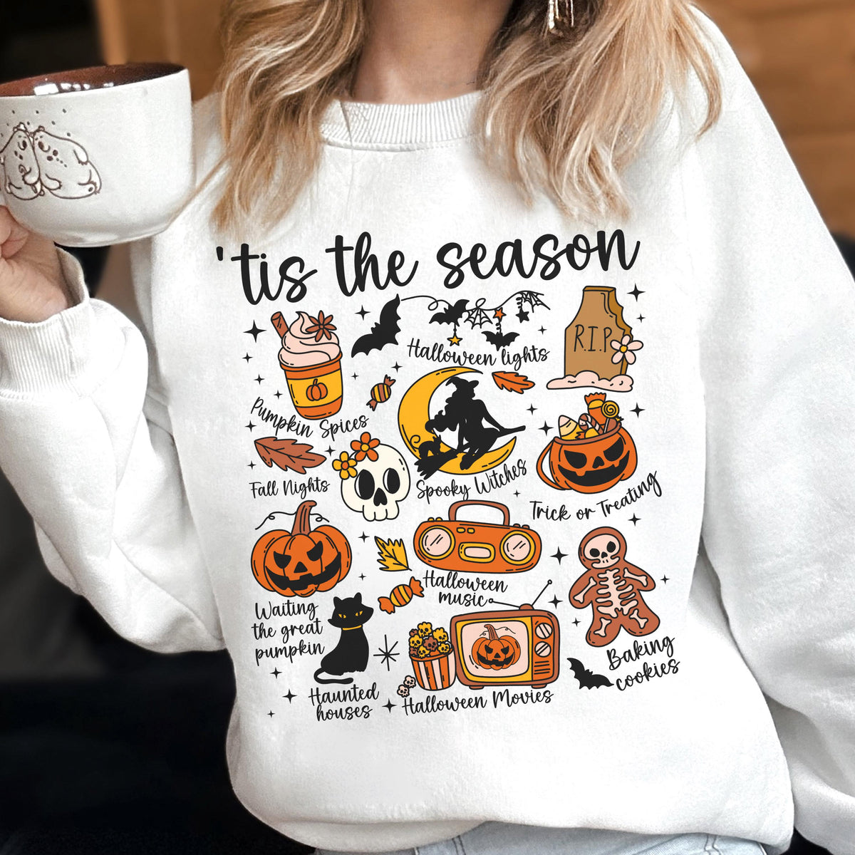 May include: White sweatshirt with a colorful Halloween-themed graphic. The design includes pumpkins, bats, a witch, and the text "'tis the season." Other elements include a skull, a black cat, and the words "Pumpkin Spices" and "Trick or Treating."