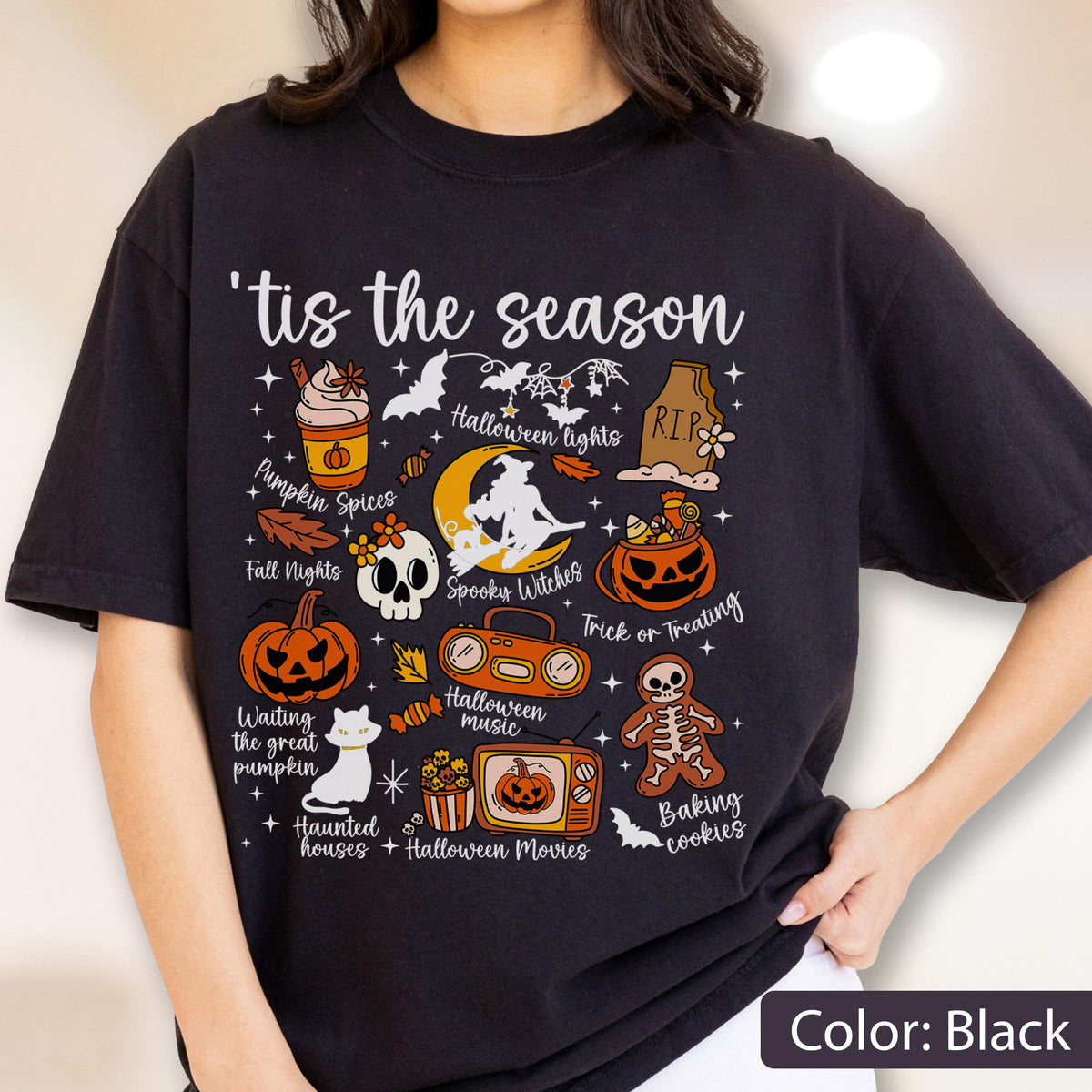 May include: A black t-shirt featuring the text 'tis the season and various Halloween-themed illustrations including a pumpkin spice drink, a tombstone, a witch on a moon, a jack-o'-lantern, a boombox, a skeleton cookie, a cat, and a television.