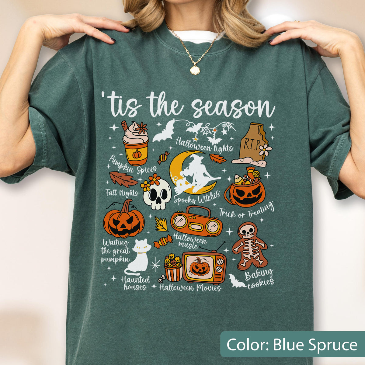 May include: A blue spruce t-shirt featuring the text 'tis the season and various Halloween-themed illustrations including a pumpkin, a skull, a witch on a moon, a jack-o'-lantern, a boombox, a television, a skeleton cookie, and a white cat.
