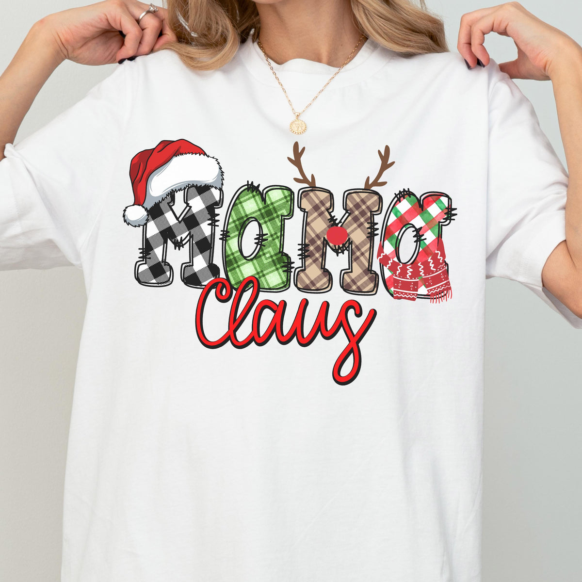 May include: White t-shirt featuring the text "Mama Claus" in a festive design. The letters are decorated with a Santa hat, plaid patterns, antlers, and a scarf, all in Christmas colors. The word "Claus" is in a red script font.