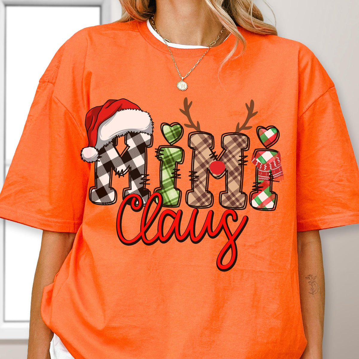 May include: Bright orange t-shirt with the words "Mimi Claus" in a festive design. The letters are decorated with plaid patterns, a Santa hat, reindeer antlers, and hearts. The word "Claus" is in a red script font.