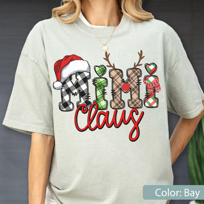 May include: A light sage green t-shirt featuring the text "Mimi Claus" in a decorative font. The letters are styled with plaid patterns, a red Santa hat, reindeer antlers, a red nose, a green heart, and a red and green scarf graphic.
