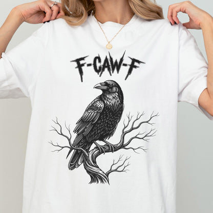 May include: White t-shirt featuring a detailed black raven perched on a tree branch. The text "F-CAW-F" is printed above the raven. The design is a graphic illustration.